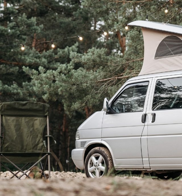 campervan in the woods with camping chairs out front and fairy lights hanging up